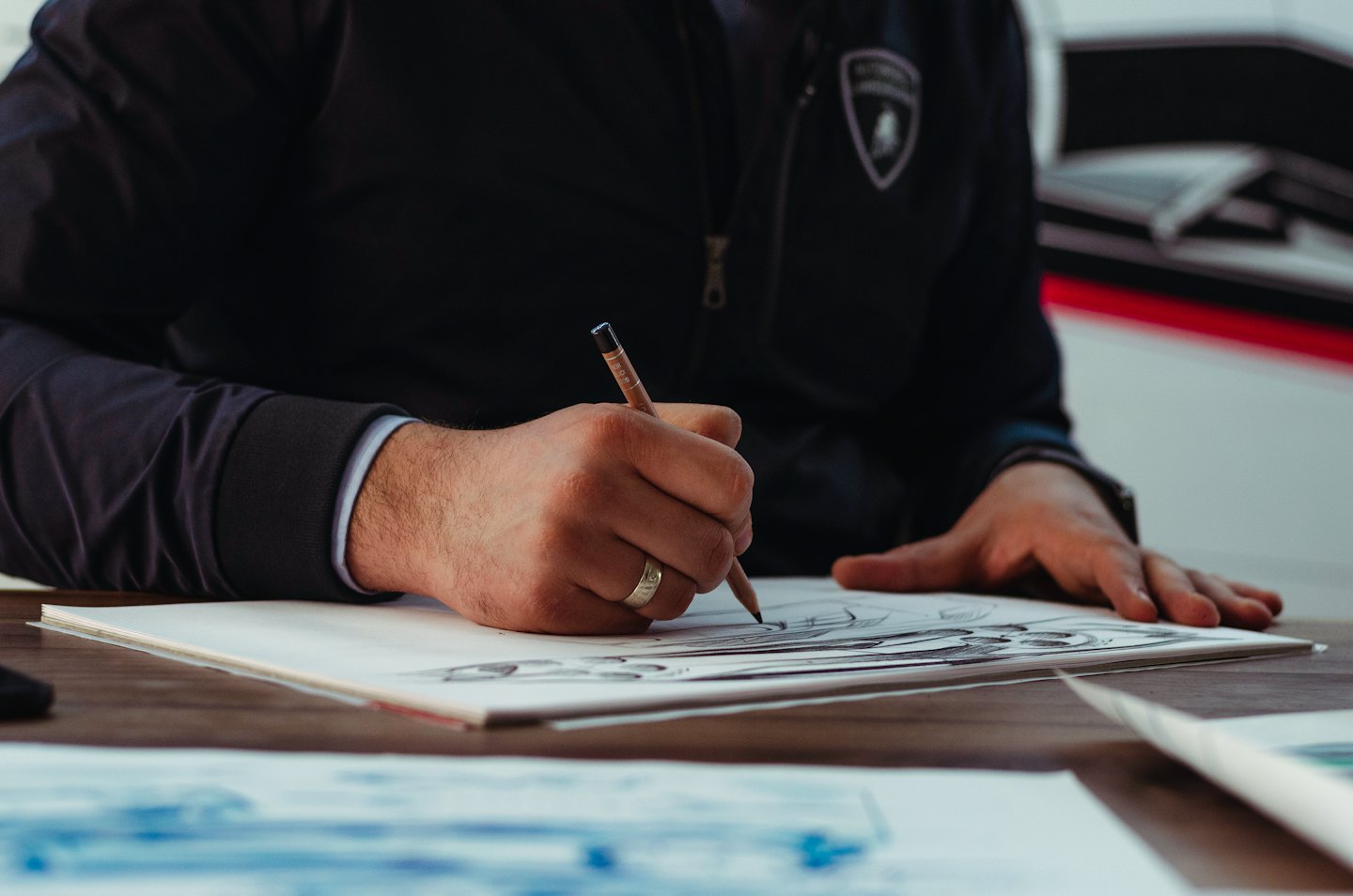 Designer's hands sketch a vehicle on white paper with a pencil.