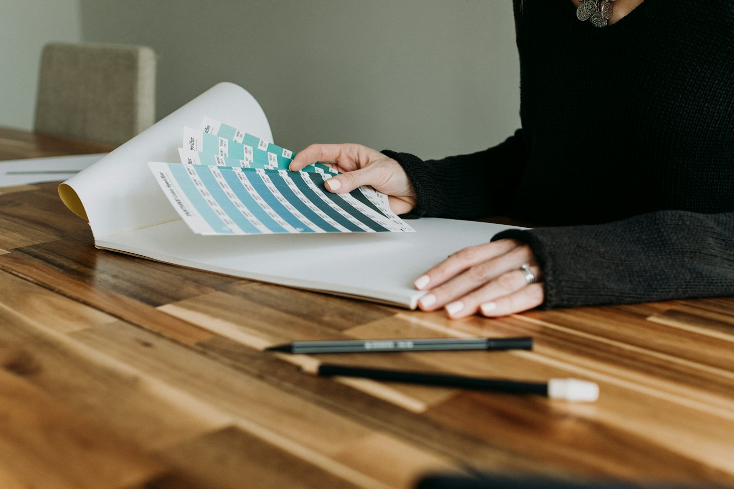 Creative hands holding open a Pantone color swatch book at a wooden table.